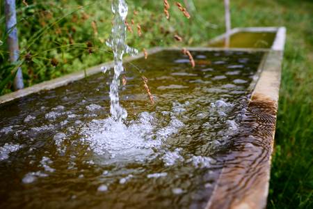 Frisches sprudelndes Wasser in einem kleinen Holzbrunnen auf der Alm  2019